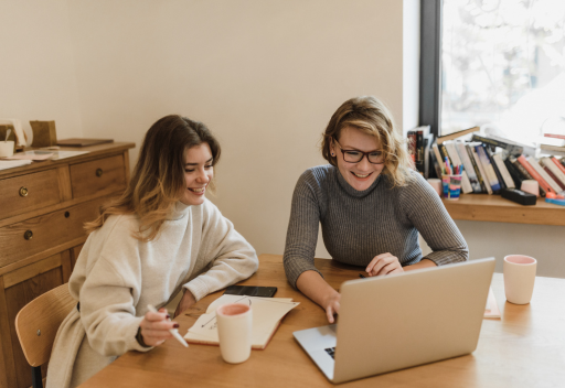 Two women wearing sweaters smile and look at the computer.